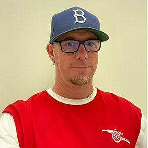 White man wearing glasses and a blue baseball cap and red shirt
